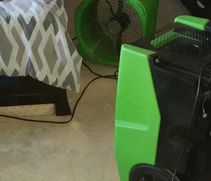 green and black SERVPRO vacuum and carpet cleaning equipment. Black bed with comforter in the corner and dresser on the right