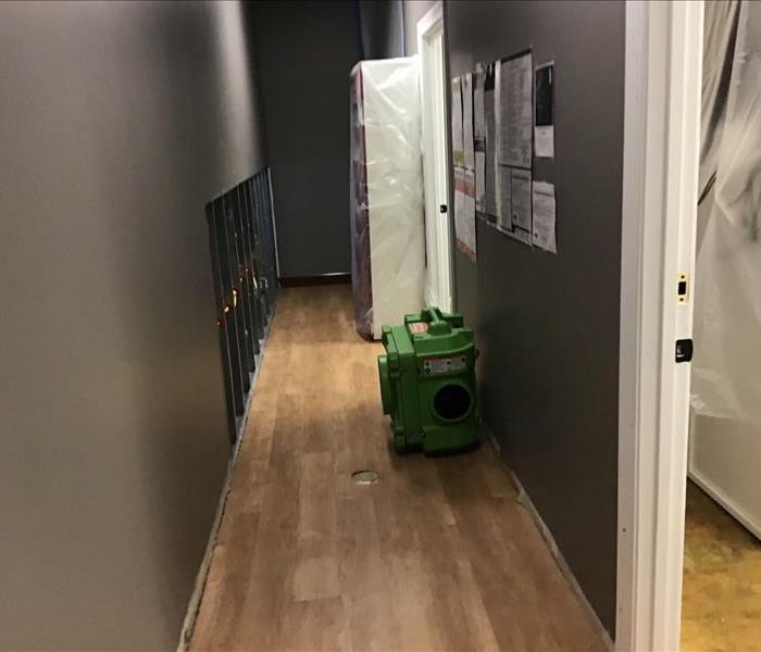 wooden hallway of office with SERVPRO equipment to the right and grey painted walls. Employee information on wall.