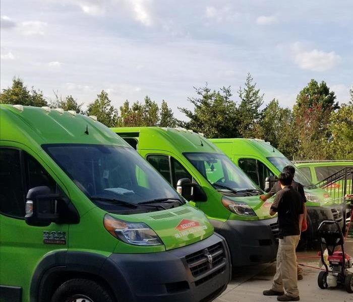 row of green SERVPRO vans on cement with two employees inspecting them. 