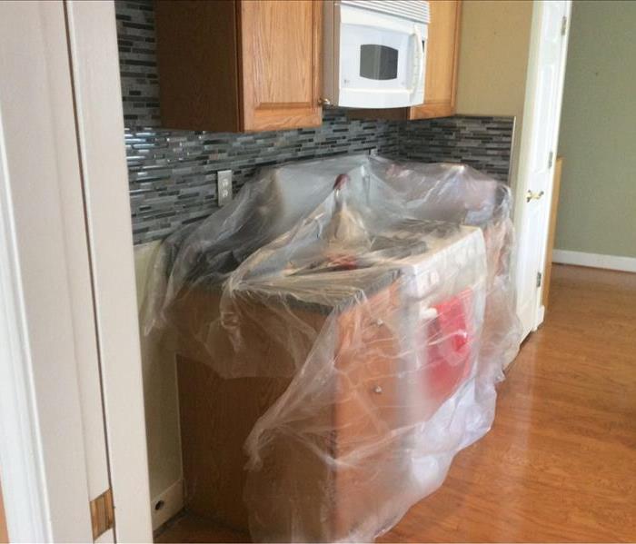 plastic wrapped portion of kitchen counter tops with wood flooring.
