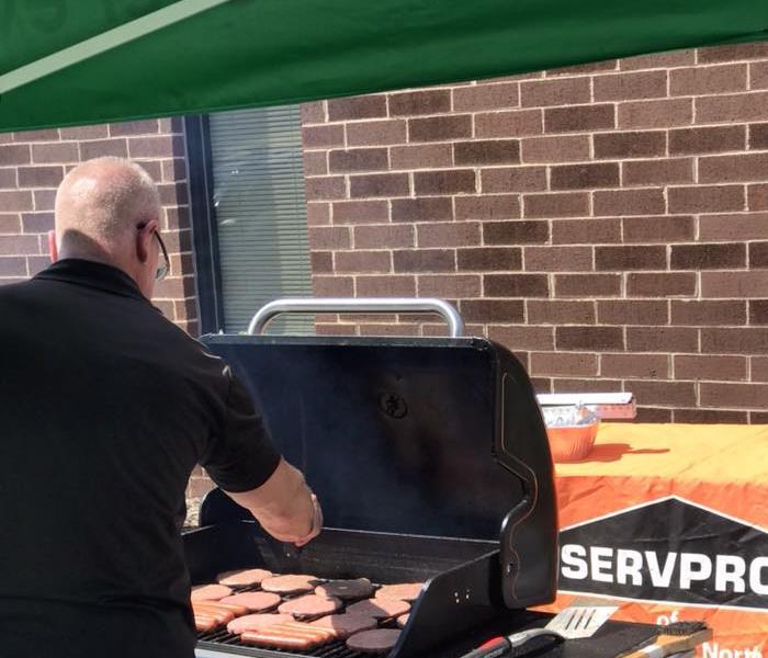 Male SERVPRO employee grilling burgers on grill in front of brick building.