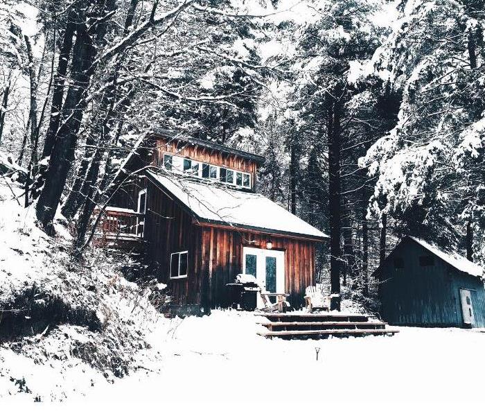 snow covering wooden house in the forrest with a blue house next to it.