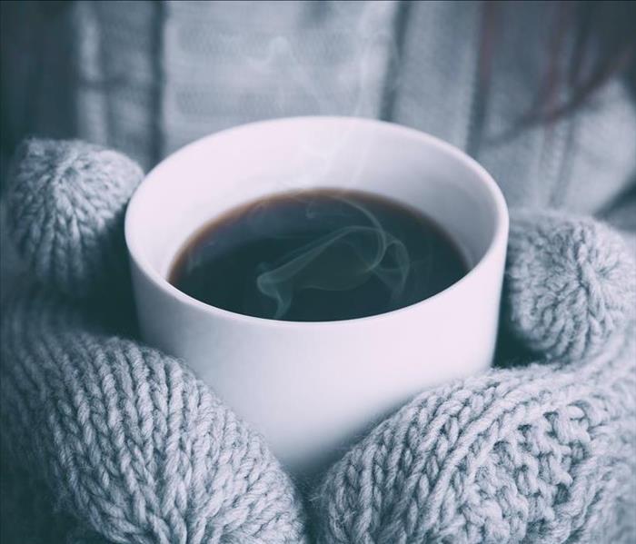A gloved woman holds a hot cup of coffee